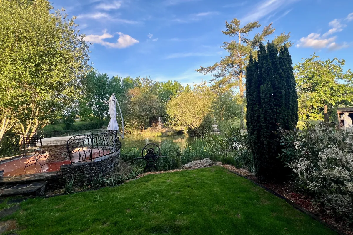 The garden pond lined with trees and flower beds, in Corné